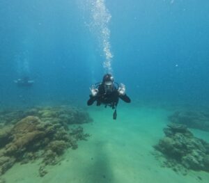 Scuba diver underwater near a rocky coral seabed, bubbles rising from the diver's mouth.